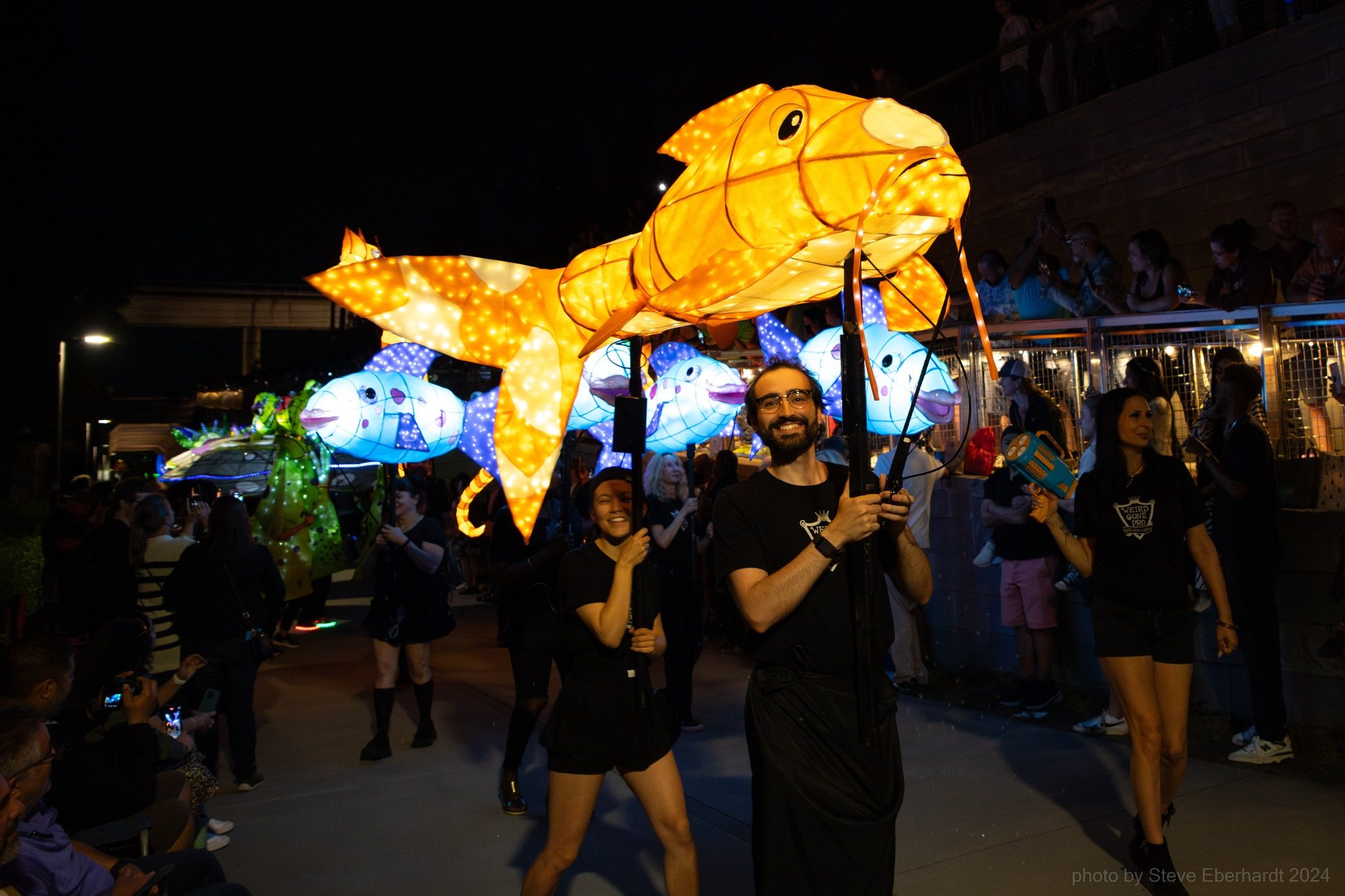 Colita, our giant glowing orange catfish lantern, carried through a night parade.